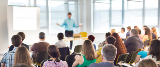 Seminarsituation, in der viele Menschen einem Referenten zuhören
